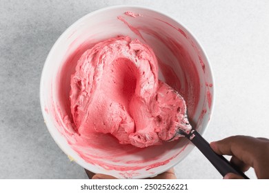 Overhead view of buttercream being colored pink, top view of american buttercream in a white bowl being colored pink, process of making american buttercream