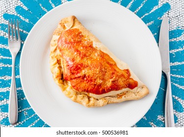 Overhead view of a calzone, a type of folded pizza, on a white plate