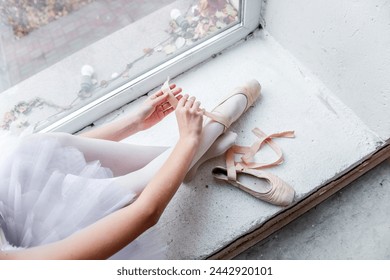 Overhead view captures a ballerina seated by a bright window, meticulously tying her pointe shoes in preparation for dance, surrounded by the urban scape outside. - Powered by Shutterstock