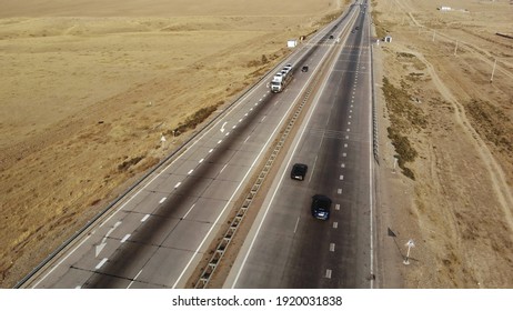 An Overhead View Of A Car Driving Along An Empty Highway On A Sunny Day. The Drone Follows The Vehicle Along A Narrow Asphalt Road. Car Driving Through The Desert