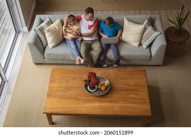 Overhead View Of Caucasian Father And Two Sons Using Laptop And Digital Tablet At Home. Childhood, Technology And Home Concept