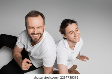 overhead view of cheerful father and teenage son in white t-shirts smiling on grey