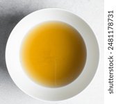 Overhead view of chicken broth in a white bowl, top view of cooked chicken beef broth, process of making broth