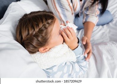 Overhead View Of Child Sneezing In Paper Napkin Near Mother On Blurred Background