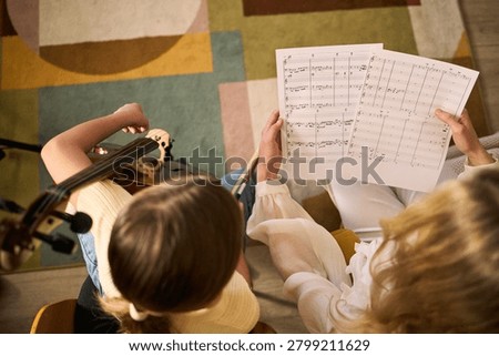 Overhead view of child studying sheet music and playing violin with teacher guidance, practicing music education and skill development. Useful for music school, tutoring, arts learning