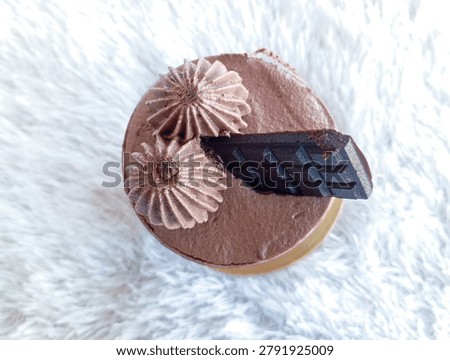 Overhead view of a chocolate dessert featuring cream rosettes and dark chocolate garnish on a textured white surface.