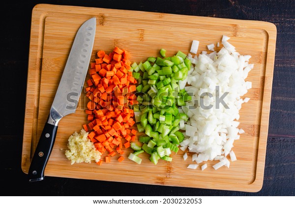 Overhead View of Chopped\
Vegetables on a Bamboo Cutting Board: Finely chopped carrots,\
celery, onions, and garlic on a wooden cutting board with a santoku\
knife