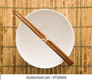 Overhead View Of Chopsticks Lying Across An Empty Bowl On A Bamboo Mat. Horizontal Format.