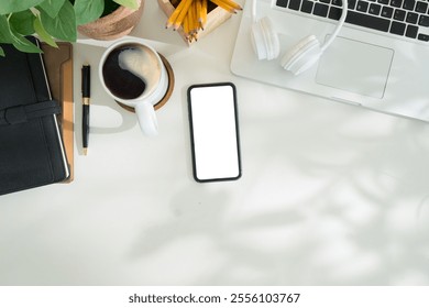 Overhead view of clean and organized desk with blank smartphone, coffee, stationery and a laptop, for digital and productivity themes. - Powered by Shutterstock