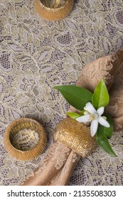 Overhead View Of A Cloth Napkin With Gold Colored Beaded Napkin Rings And A Floral Accent, Arranged On A Lace Tablecloth. Concept Of Holiday Or Entertaining With Copy Space.