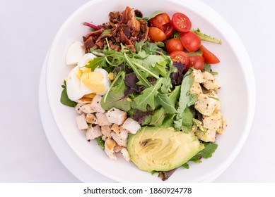 Overhead View Of Cobb Salad Piled High With Sliced Avocado, Tomato, Chicken, Hard Boiled Egg, And Arrugula.