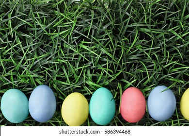 Overhead View Of Colorful Easter Eggs Lined Up In A Row Over A Background Of Grass. Flat Lay Style.