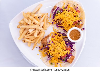 Overhead View Of Combo Plate Of Fish Tacos Topped With Shredded Cheese Served With French Fries And Salsa.