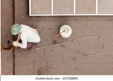 Overhead View Of Construction Worker Using Propane Torch With Gas Cylinder To Patch Tar Paper On Flat Roof