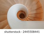 An overhead view of a contemporary spiral staircase with a flawless white balustrade and warm wooden steps that elegantly twist downwards, creating a mesmerizing architectural pattern.