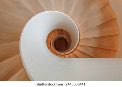 An overhead view of a contemporary spiral staircase with a flawless white balustrade and warm wooden steps that elegantly twist downwards, creating a mesmerizing architectural pattern. - Powered by Shutterstock