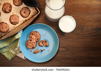 Overhead View Of Cookie Sheet And Plate Of Chocolate Chip Cookies Warm From The Oven With Glass Of Cold Milk On Vintage Wood Table