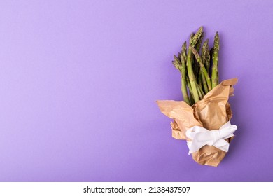 Overhead view of copy space by asparagus bunch tied in paper with ribbon on purple background. unaltered, food, healthy eating and organic concept.