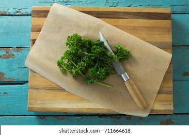 Overhead View Of Coriander Leaves, Wax Paper And Knife On Chopping Board