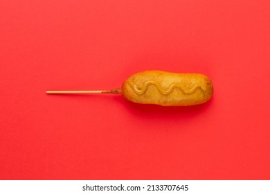 Overhead View Of Corn Dog With Mustered Sauce Over Skewer On Red Background With Copy Space. Unaltered, Copy Space, Unhealthy Food, Meat, Sausage And Fried Food.