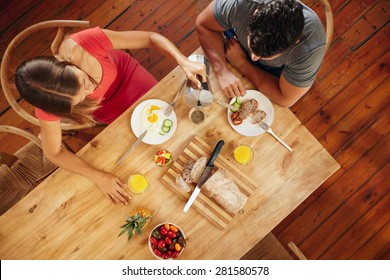 Overhead View Of Couple Having Morning Breakfast In Kitchen With Woman Serving Coffee To Man.