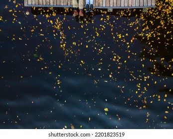 Overhead View Of Couple Legs At The Wooden Pier Lake Water With Yellow Leaves Copy Space