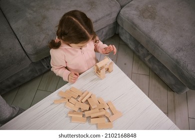 Overhead View Of Creative Preschool Child, Concentrated Baby Girl On Building With Wooden Blocks Bricks. Educational Board Game And Developmental Smart Pastime. Fine Motor Skill Development Concept
