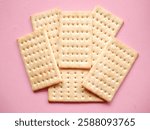 An overhead view of crisp, rectangular crackers arranged on a soft pink background. The crackers have making them perfect for various culinary uses, snacks, or as an ingredient in recipes.