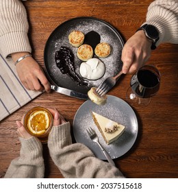 Overhead View Of Crop Couple Eating Cheese Pancakes And Carrot Cake Desserts During Date In Cafe While Sitting At Table With Alcohol Drinks In Autumn 