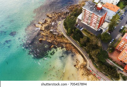 Overhead View Of Crowd Of Swimmers Going For A Regular Race Swim At Manly Beach In Sydney, Australia, Around Coastal Cliff And Residential Houses.