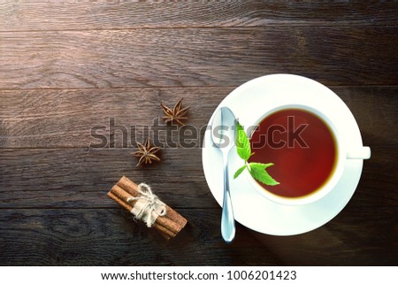 Overhead view of a cup of tea with cinnamom, mint leaves and fruits of star anise.