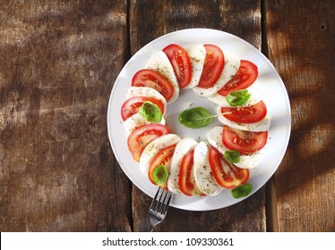 Overhead View Of A Decorative Sliced Tomato And Cheese Salad Arranged Alternately Around A Plate On An Old Textured Wooden Table