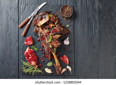 Overhead View Of Delicious Roast Tender Leg Of Lamb Served With Pomegranate Seeds, Mint Leaves, Spices And Rosemary On A Black Slate Plate On A Wooden Table,view From Above, Copy Space, Flatlay