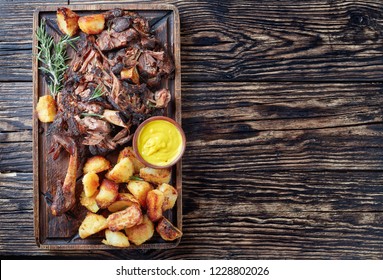 Overhead View Of Delicious Slow Roast Tender Leg Of Lamb Pulled Off The Bones And  Served With Crispy Roast Potatoes On A Wooden Tray On A Rustic Wooden Table,view From Above, Copy Space, Flatlay