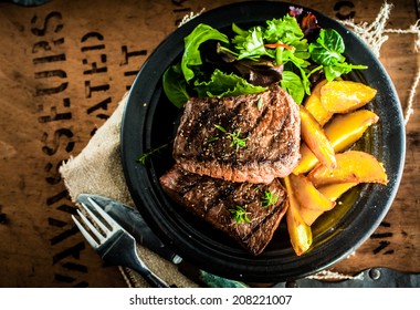 Overhead View Of Delicious,grilled Beef Steak With Roasted Pumpkin And Fresh Green Herb Salad On An Old Wooden Packing Case With Printed Text