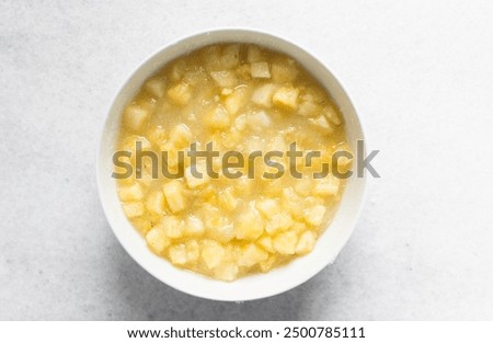 Overhead view of diced pineapple and sugar being mixed together in a white bowl, process of making pineapple cheong or pineapple syrup