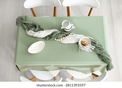 Overhead view of a dining table set with a sage green tablecloth, white chairs, and modern tableware