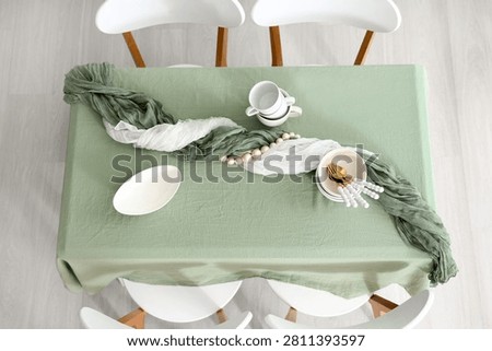 Overhead view of a dining table set with a sage green tablecloth, white chairs, and modern tableware