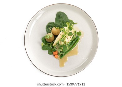 Overhead View Of A Dinner Plate Of Baked Filet Of Halibut Or Sea Bass Fish Garnished With Spinach And Pea Shoots Isolated On White