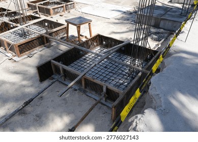 An overhead view displays multiple square wooden formworks, each containing an intricate steel rebar cage, prepared for the next stage of concrete foundation work.
