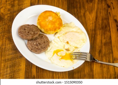 Overhead View Of Eggs Over Easy With Sausage And Buttered Biscuit On Rustic Wood Table