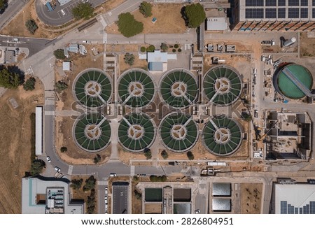 Overhead view of eight circular flocculation-decantation clarifiers at an industrial drinking water treatment facility, surrounded by roads, solar panels and infrastructure