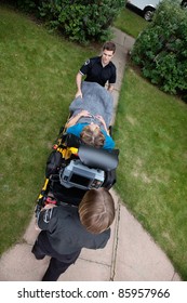 Overhead View Of Emergency Medical Team Pushing Senior Woman On Stretcher.  Shallow DOF Sharp Focus On Patient