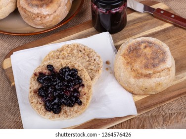 Overhead View Of An English Muffin Cut In Half And Spread With Blueberry Preserves On A Napkin Along With A Whole Muffin And Jar Of Preserves