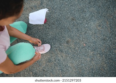 Overhead View Of A Female Athlete In Colorful Sportswear Tying Shoelaces On The Sportsground, Getting Ready For Outdoor Workout