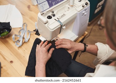 Overhead view of a female fashion designer dressmaker tailor seamstress sewing clothes on sewing machine in a tailoring atelier. Creating new garment, fashion designer business start-up concept