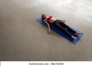 Overhead View Of Fit Young Female Relaxing On Yoga Mat. Healthy Woman In Savasana Pose On Concrete Grey Floor With Copy Space