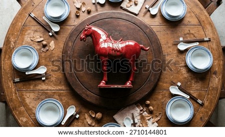 Overhead view of a formal dinner setting on a round Chinese table with a central red glazed horse statue, ready for a feast.