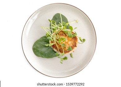 Overhead View Of A Fried Crab Cake Or Fish Cake Garnished With Spinach And Pea Shoots Isolated On White