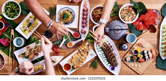 Overhead View Of Friends Eating Traditional Japanese Food Dishes Served On The Table. Set Of Sushi, Rolls, Spaghetti Pasta, Edamame, Gyozas And Tuna Tataki.